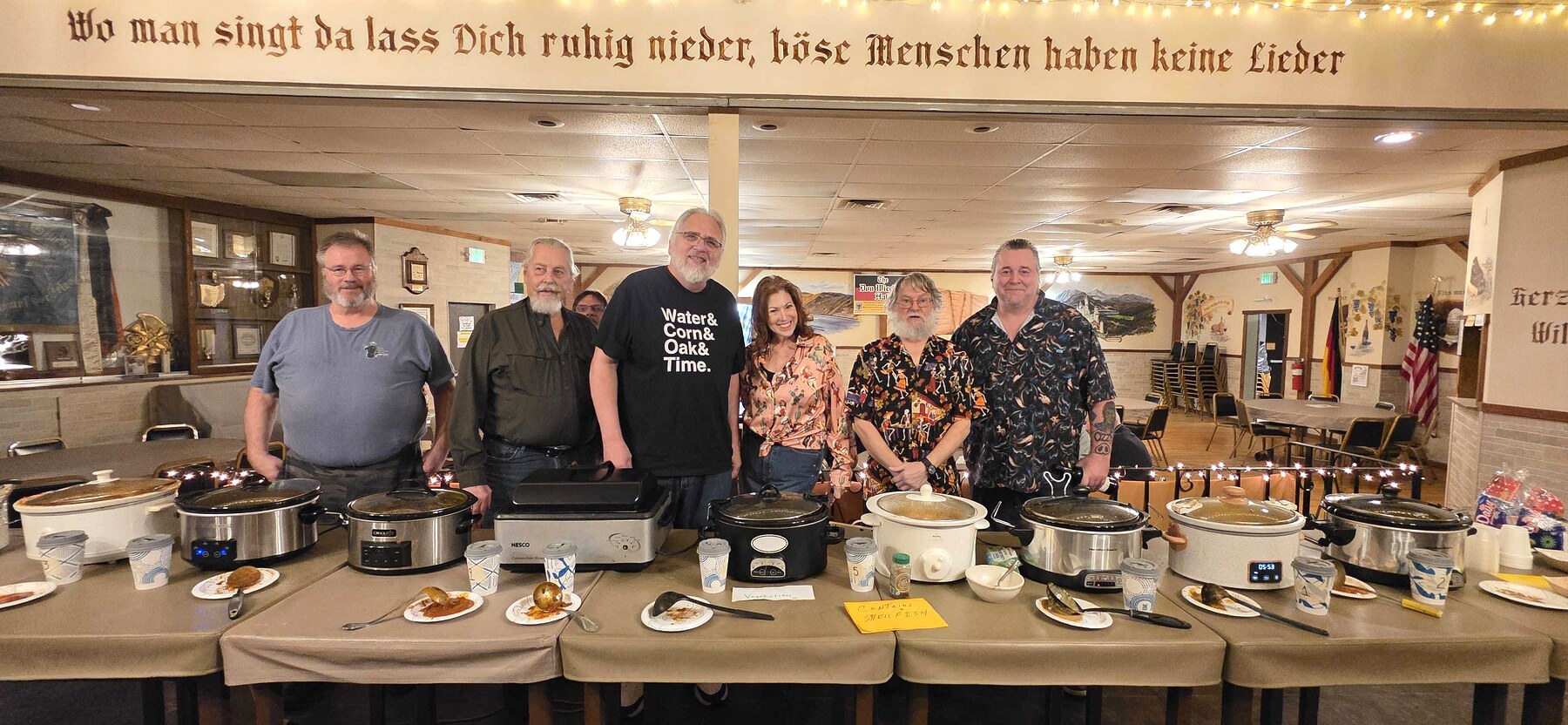 All nine Chili Cook Off contestants standing behind their crockpots at Cleveland Maennerchor